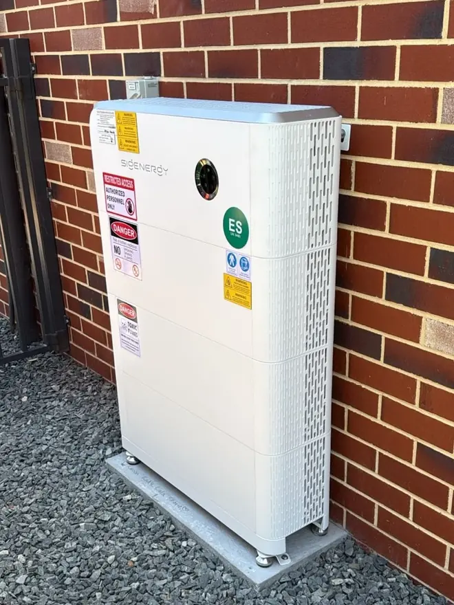Wall-mounted home battery installed against red brickwork